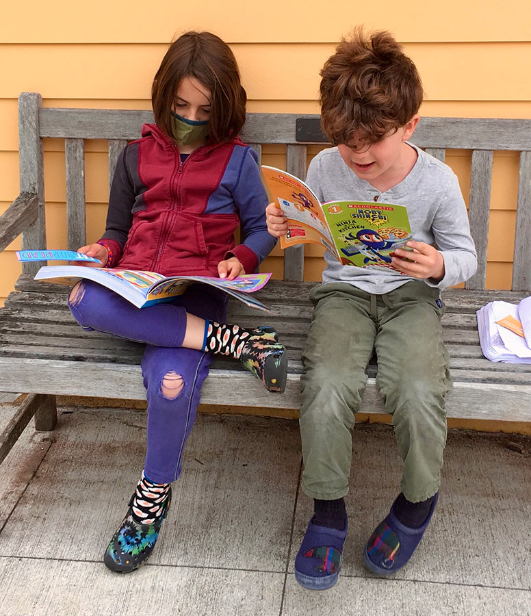 Two elementary-age students reading next to each other on a bench