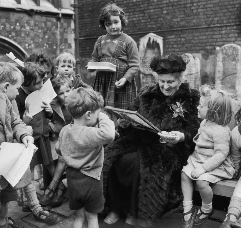 Black and white image of Maria Montessori reading to toddlers