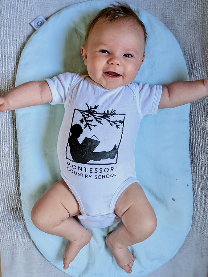Baby smiling at the camera wearing a Montessori Country School onesie